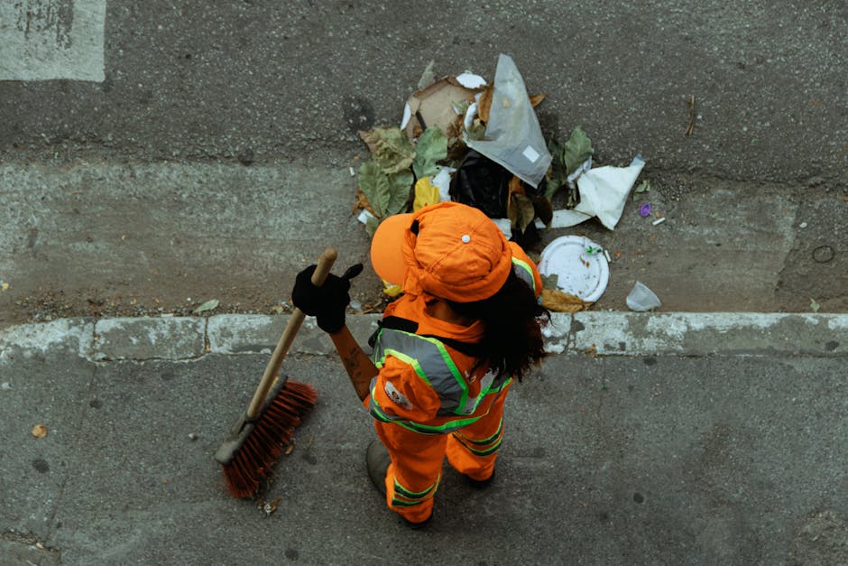 A black wheeled rubbish bin with the name 'ST. JOHN'S' printed on the front, positioned on a quiet suburban street at night. The bin contains various discarded items, including flattened cardboard and